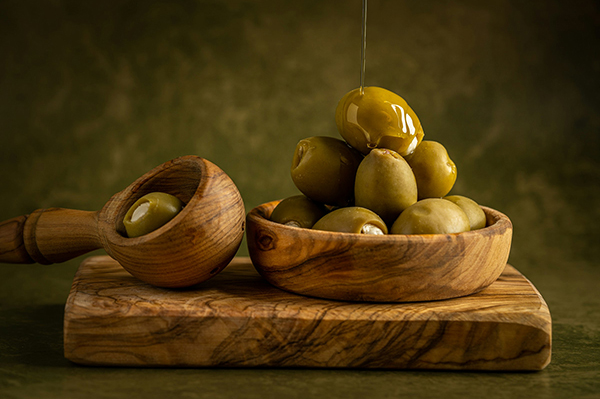 Golden green olives drizzled in olive oil placed on wooden board
